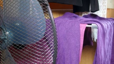 Ein Ventilator bläst Luft auf feuchte, lila Wäsche, die auf einem Gestell in einem Raum hängt, um sie im Winter zu trocknen.