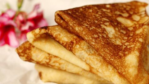 Knusprige Haferflocken-Pfannkuchen liegen gestapelt auf weißem Papier, umgeben von einer blühenden, bunten Blume.