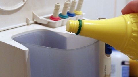 Eine Hand hält eine gelbe Flasche über eine Munddusche, während sie eine Reinigungslösung in den Behälter einfüllt.
