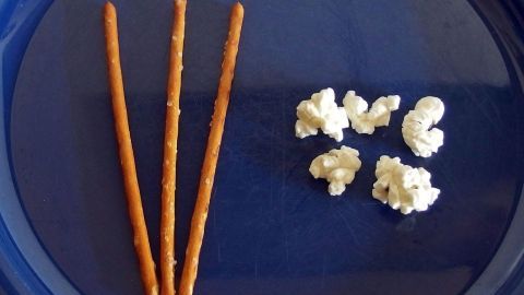 Drei Brezeln liegen neben einer Gruppe von Popcorn auf einem blauen Teller, ideal für interaktives Zählen mit Kindern.
