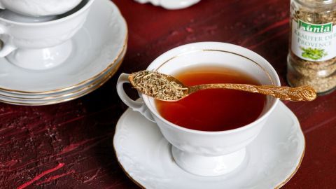 Ein Teeteller mit einer Tasse Kräutertee steht auf einem Tisch, umgeben von weiteren Tassen und einer Gewürzdose.