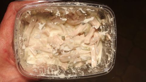 Eine Hand hält einen durchsichtigen Behälter mit einem schimmligen, unappetitlichen Inhalt, der unangenehme Gerüche im Kühlschrank verursachen kann.