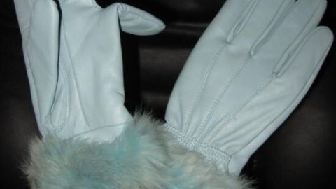 Zwei elegante, glatte Lederhandschuhe mit einem dunkeltürkisen Pelzbesatz stehen stilvoll in einer weißen Kanne vor schwarzem Hintergrund.