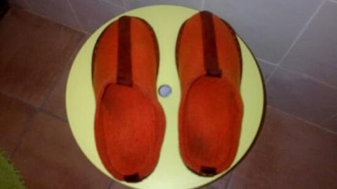 Orange Filzpantoffeln liegen auf einem kleinen, runden, gelben Tisch vor einem gefliesten Hintergrund auf dem Boden.
