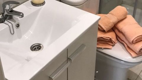 Ein modernes Waschbecken mit einem Seifenspender steht neben einer Toilette, während orangefarbene Handtücher bereitliegen.