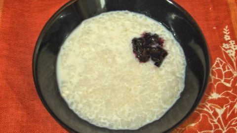 Eine Schüssel mit cremigem Milchreis steht auf einem rustikalen Tisch. Ein wenig Fruchtkompott ziert die Oberfläche.