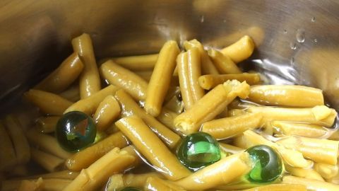Grüne Bohnen und bunte Kugeln schwimmen in einem Topf, während sie für ein Gericht gekocht werden, um Anbrennen zu vermeiden.