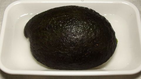 Eine gesamte Avocado liegt in einer weißen Schale. Sie sieht frisch aus und wird zur Aufbewahrung vorbereitet.