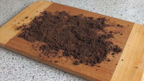 Ein Schneidebrett kann man mit Kaffeesatz reinigen. Das ist preisgünstig und funktioniert sehr gut. Ein Holzschneidebrett mit altem Kaffeesatz ist auf einer hellen, glatten Oberfläche sichtbar, bereit zum Reinigen.