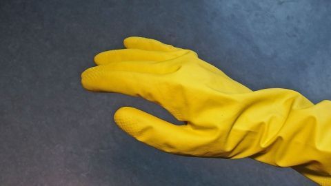 Gelbe Gummihandschuhe liegen auf einem dunklen Tisch, bereit für die Anwendung in der Handpflege bei Arbeiten.