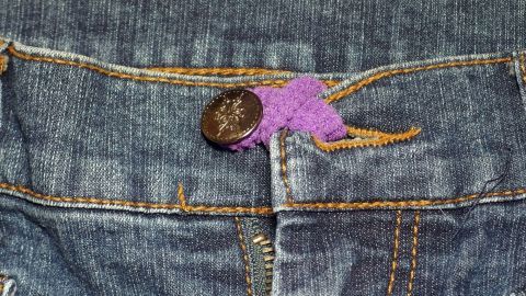 Ein lila Zopfgummi hält die Jeans offen, um eine bessere Passform zu ermöglichen, während eine Diät begonnen wird.