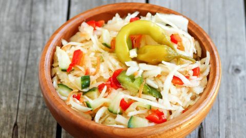 Ein Holzschüssel mit frischem Krautsalat, angereichert mit buntem Gemüse, steht auf einer rustikalen Holzoberfläche.