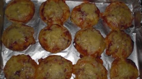 Mini-Pizzas liegen frisch gebacken auf einem mit Alufolie belegten Backblech im Ofen.
