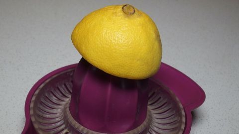 Eine gelbe Zitrone liegt auf einem Entsafter, bereit zum Auspressen auf einer hellen Arbeitsfläche.