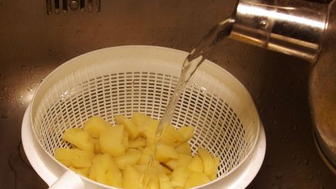 Keine verklebten Kartoffelscheiben bei der Zubereitung von Kartoffelsalat. Schälchen mit Kartoffelscheiben wird mit heißem Wasser übergossen, um "verklebte" Scheiben zu lösen, im Waschbecken.