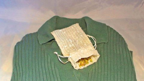 Ein grüner Pullover liegt flach mit einem kleinen Säckchen aus Naturmaterial, das duftende Zutaten enthält.