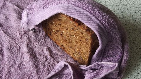 Ein Stück altes Brot liegt teilweise eingewickelt in einem lilafarbenen Tuch auf einer grauen Arbeitsplatte.