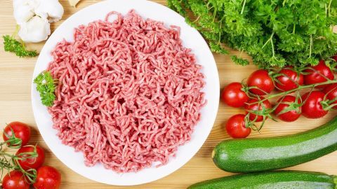 Hackfleisch liegt frisch in einer Schale und wird von Tomaten, Zucchini und Kräutern umgeben, ideal für leichte Gerichte.