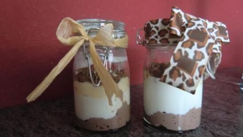 Zwei dekorativ servierte Dessertgläser mit verschiedenen Schichten und bunten Bändern stehen auf einer dunklen Oberfläche.
