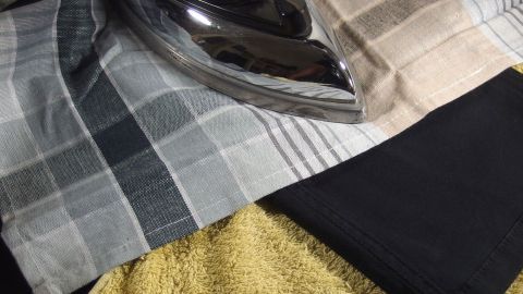 Schwarze Jeans liegen auf einem gelben Handtuch, während ein Bügeleisen darauf platziert ist, bereit zu bügeln.