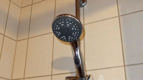 Ein Duschkopf ist an der Wand montiert und spritzt Wasser, während die Fliesen im Hintergrund die Dusche umgeben.