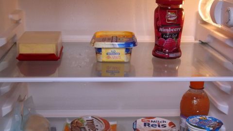 Ein Kühlschrank steht geöffnet und zeigt verschiedene Lebensmittel wie Butter, Marmelade und Getränke auf den Regalen.