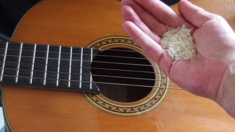 Eine Hand hält Staub, während eine Gitarre im Hintergrund steht, wobei der Staub von der Oberfläche entfernt wird.