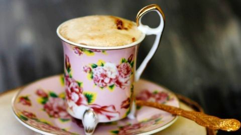 Ein feines Kaffeetässchen aus Porzellan mit Blumenmuster steht auf einem Holzuntergrund, umgeben von sanftem Licht.