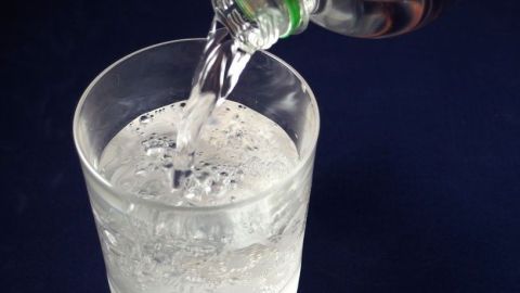 Ein Glas Wasser wird gefüllt, während sprudelnde Blasen an der Oberfläche entstehen, auf einem dunklen Hintergrund.