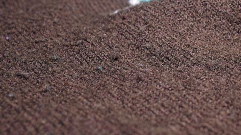 Ein brauner Wollpullover zeigt feine Knoten, die mithilfe einer Kleiderbürste sanft entfernt werden.