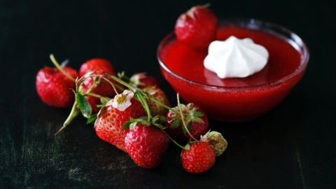 Eine Schüssel Erdbeer-Kaltschale mit Sahne steht auf einem dunklen Untergrund, umgeben von frischen Erdbeeren.