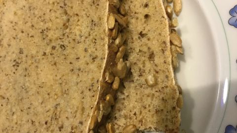 Zwei Scheiben Weizenvollkornbrot liegen auf einem Teller, reich an Samen, angerichtet auf einem floral dekorierten Tisch.