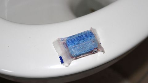 Eine Toilettentablette liegt auf dem Rand einer weißen Toilette, um blaues Toilettenwasser zu erzeugen und länger frisch zu halten.