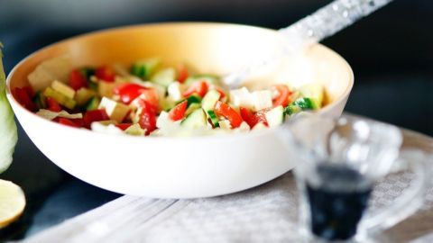 Frischer Salat in einer weißen Schüssel, garniert mit Balsamico-Dressing, auf einem Tisch mit einem Tuch.