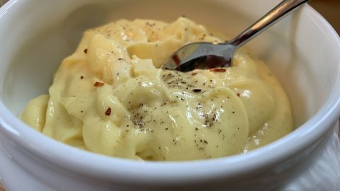 Eine Schüssel mit cremiger Trüffelmayonnaise, in der ein Löffel steckt, steht auf einer Holzoberfläche.