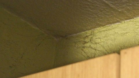 Im oberen Bereich eines Zimmers sind Spinnweben an der Decke sichtbar, die entfernt werden sollen.