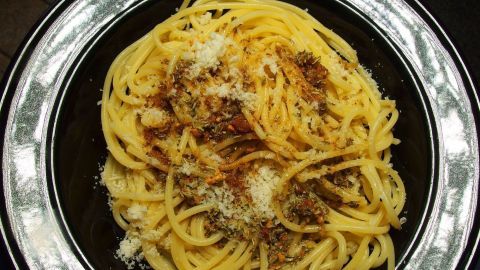 Dunkle Pasta mit schlichtem, schmelzenden Käse, garniert mit einer Rosmarin-Butter-Soße auf einem eleganten Teller.