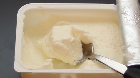 In einer offenen Schale liegt cremiger Quark, während ein Löffel hineingreift, um ihn zu entnehmen.