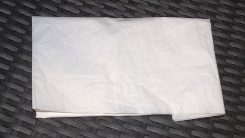 Ein Seidenpapier liegt faltig auf einer dunklen, strukturierten Oberfläche und wirkt leicht transparent und zerknittert.