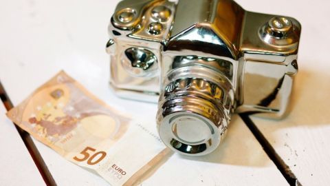 Eine glänzende Kamera liegt neben einem 50-Euro-Schein auf einer Holzoberfläche, symbolisiert Sparen beim Fotografieren.