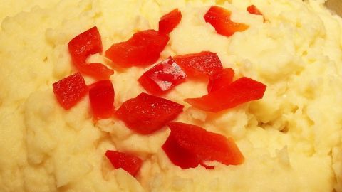 Eine cremige Portion Kartoffelpüree wird mit roten Paprikastücken garniert, appetitlich in einer warmen Küche serviert.
