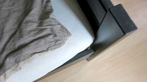 Mit diesem Trick kannst du deine alten Bettlaken als Spannbettlaken verwenden: Mach vor dem Beziehen je einen Knoten an allen vier Bettlaken-Ecken. So verrutscht das Bettlaken nicht mehr so leicht! Ein straffes Bettlaken liegt über einer Matratze in einem modernen Schlafzimmer mit einem Holzfußboden.