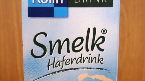 Ein Karton mit "Smelk Haferdrink" steht vor einer Holzoberfläche und präsentiert sich als laktosefreie Alternative zu Sojamilch.