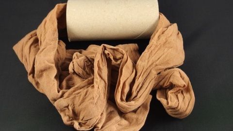 Ein zusammengerollter Pappkern liegt mittig umgeben von einer zerknüllten Strumpfhose in einem dunklen Umfeld.