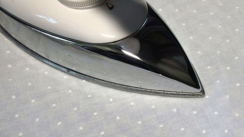 Ein Bügeleisen steht auf einem hellen, gepunkteten Stoff, bereit, um Kleidung vor Kleidermotten zu schützen.