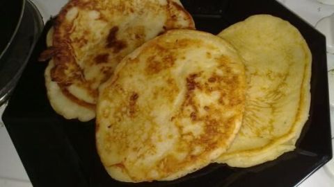 Pancakes liegen gestapelt auf einem schwarzen Teller in der Küche. Sie sind goldbraun gebraten und sehen fluffig aus.