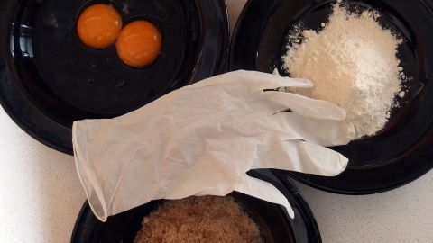 Einmalhandschuhe liegen auf einem Teller, während Eier, Zucker und Mehl in weiteren Tellern bereitstehen.