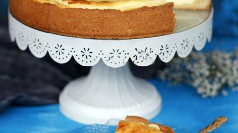 Ein Käsekuchen steht auf einem eleganten Ständer, ein Stück ist herausgeschnitten und auf einem Teller platziert.