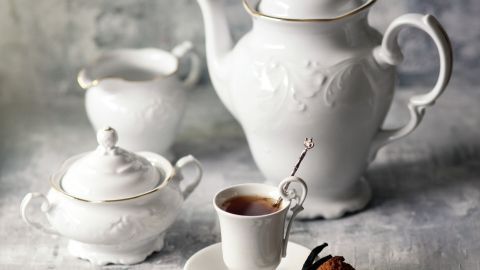 Eine elegante Teekanne mit Tassen und Zuckergefäß steht auf einem hellen, strukturierten Untergrund, bereit zum Servieren.