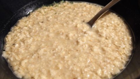 Eine Schüssel herzhaftes Haferflocken-Suppe mit einem Löffel darin steht auf einem Tisch, umgeben von neutralen Farben.